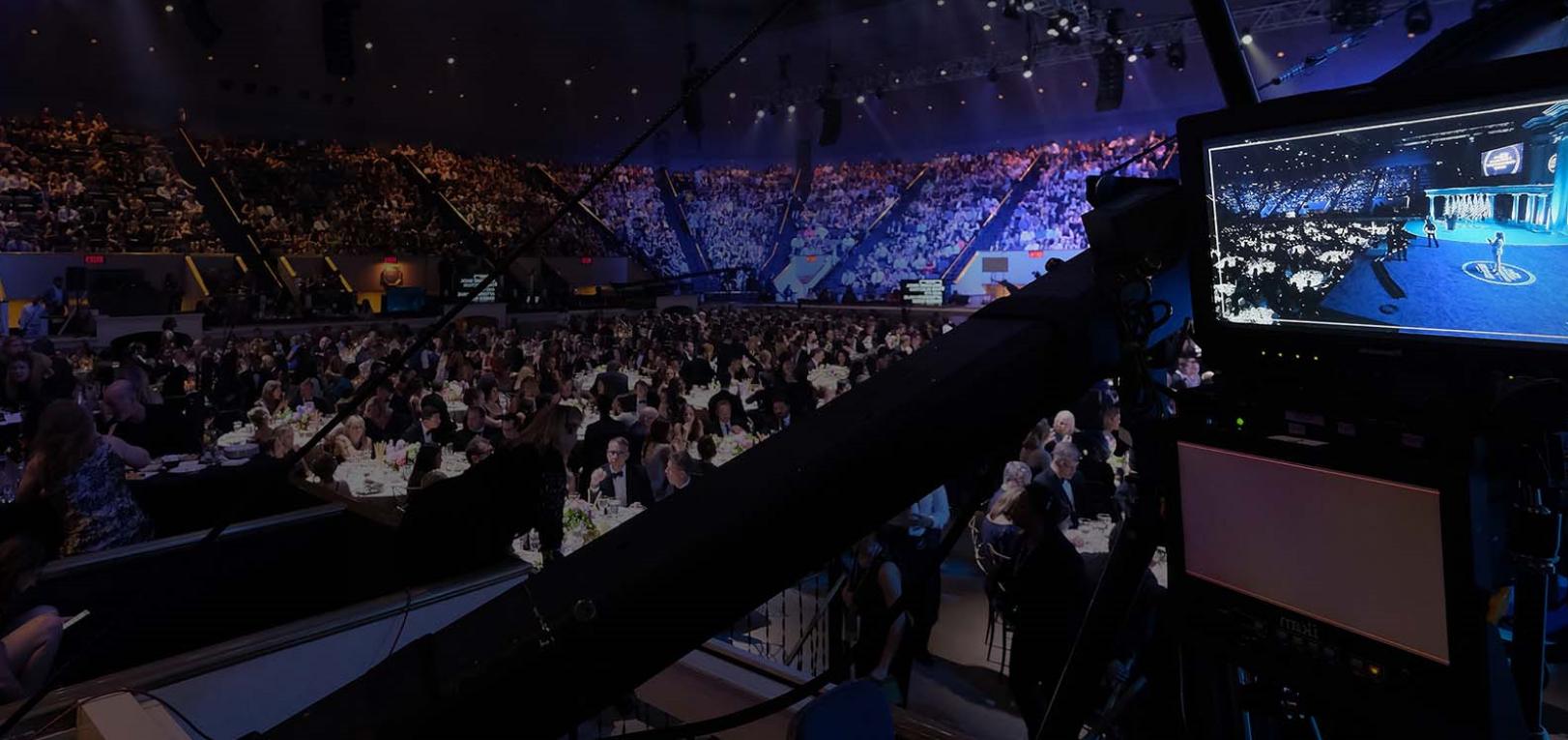 A camera position and program monitor overlooking a packed arena gala