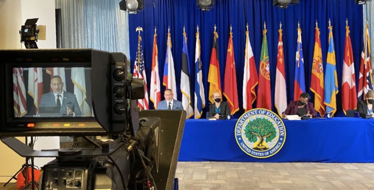 A broadcast camera framing a speaker at a U.S. Department of Education summit